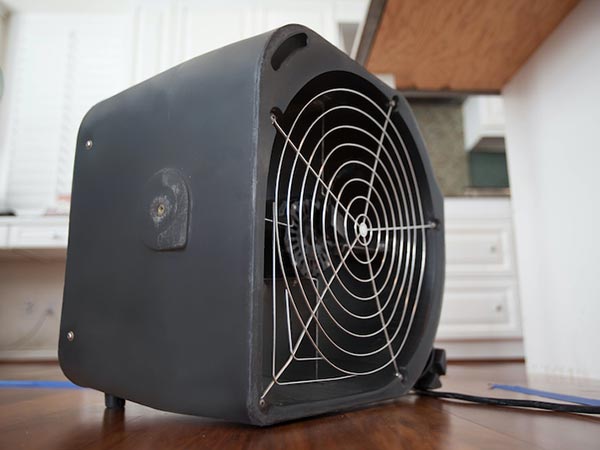 Black portable space heater with a circular metal fan guard resting on a wooden kitchen table.